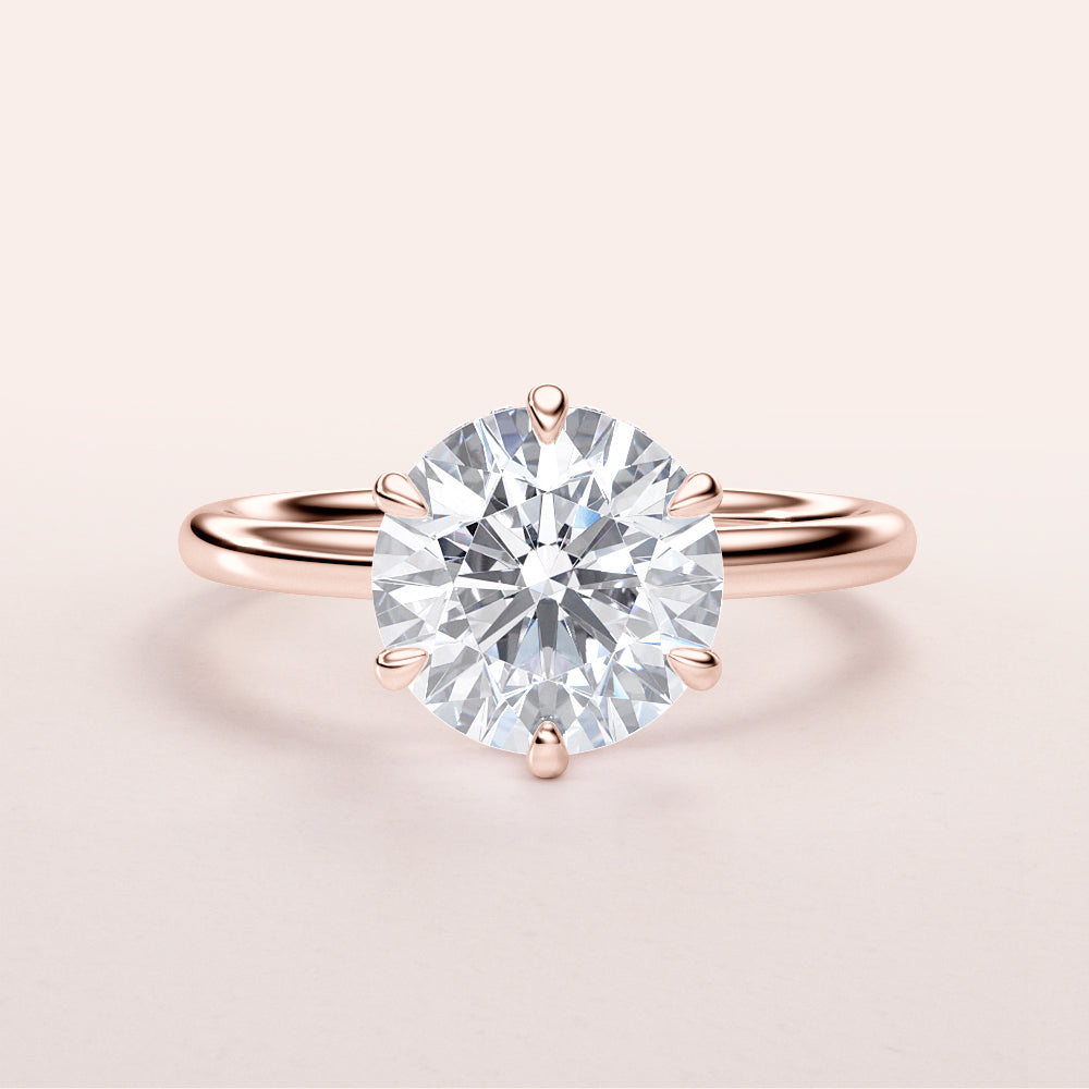 Close-up of a round brilliant-cut diamond solitaire engagement ring in rose gold, set in a sleek band, available in 14K, 18K, or platinum.