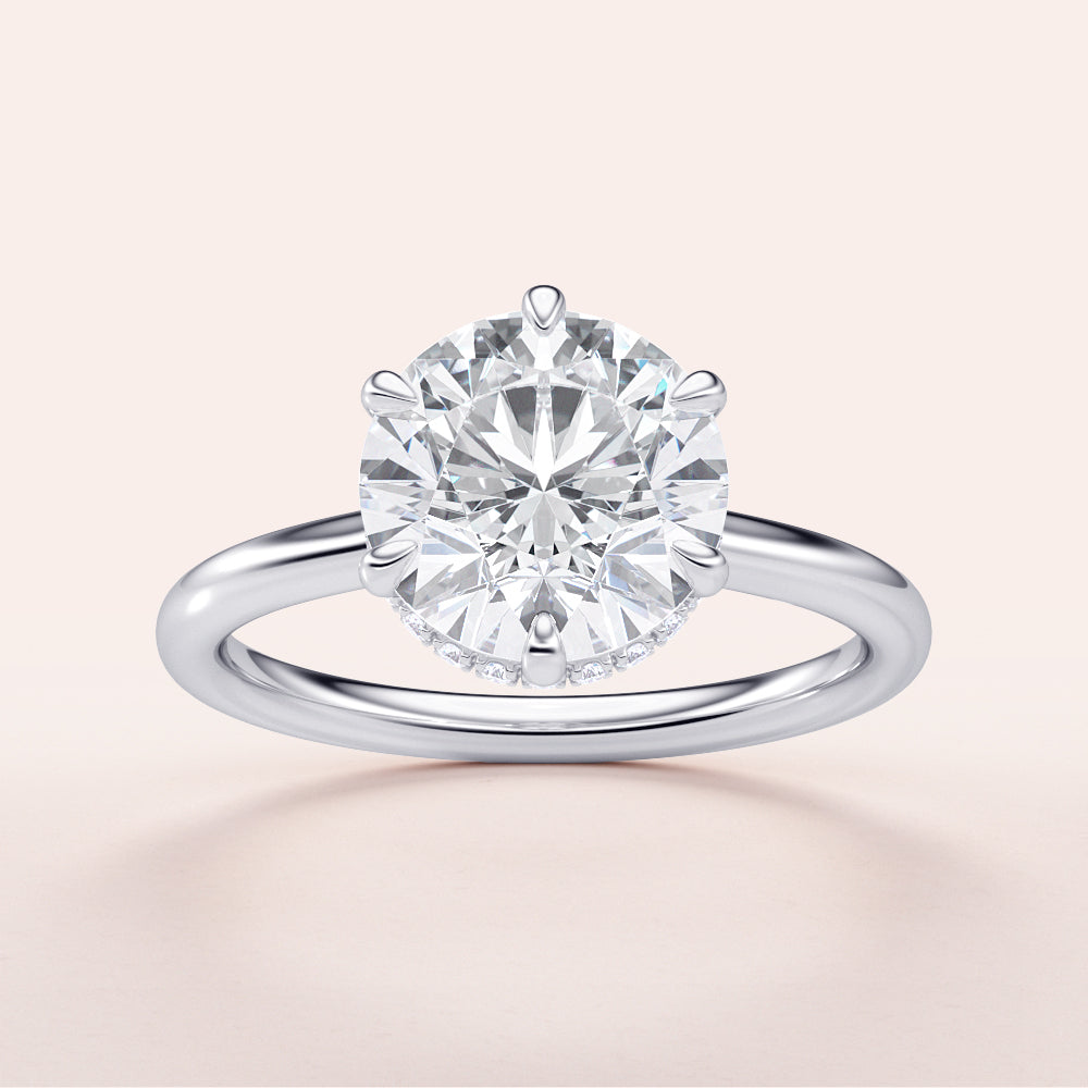 Elegant engagement ring featuring a round brilliant diamond in a 14K or 18K white gold band with hidden halo design.