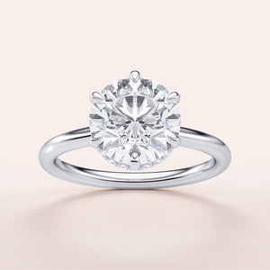 Elegant engagement ring featuring a round brilliant diamond in a 14K or 18K white gold band with hidden halo design.