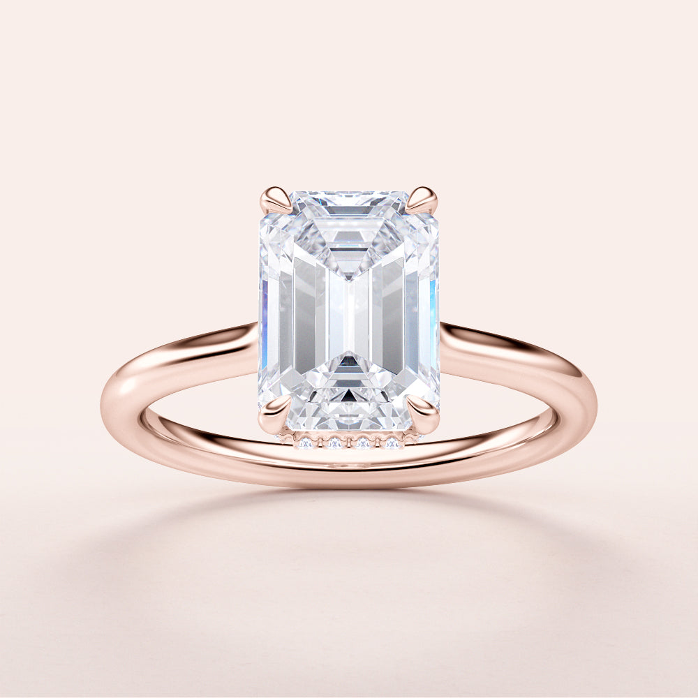 Elegant emerald engagement ring in lustrous 14K rose gold, featuring a hidden halo and plain band. Available in 18K and platinum.