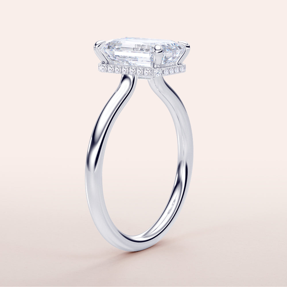 Elegant 14K/18K white gold engagement ring with radiant-cut emerald center, pave diamonds, displayed on a minimal backdrop.