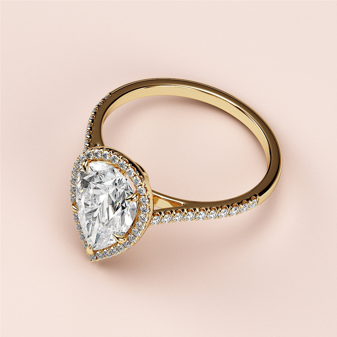 Elegant 14K or 18K yellow gold engagement ring featuring a pear-shaped diamond in a halo setting with pave band detail.
