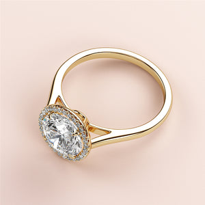 Elegant 14K or 18K yellow gold engagement ring with a round halo and cathedral band, displayed on a soft pink background.