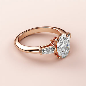 14K rose gold engagement ring with an oval diamond and tapered baguette side stones on a model's finger.