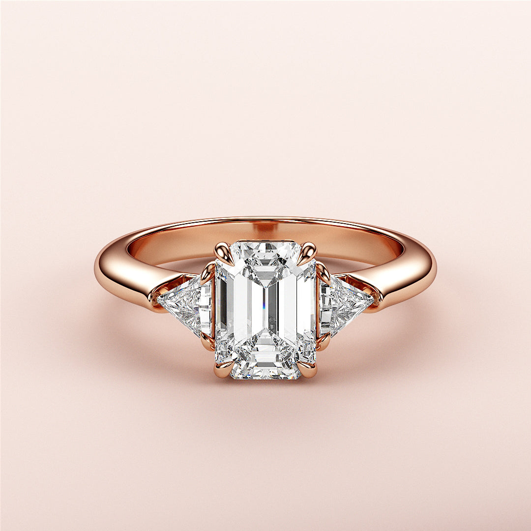 "Elegant 14K or 18K Rose Gold engagement ring featuring an emerald-cut diamond and two triangular diamonds."