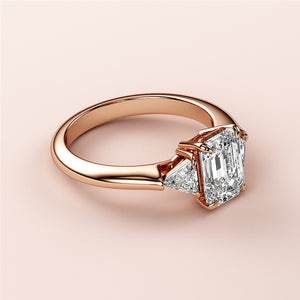 Elegant rose gold three-stone engagement ring in 14K or 18K gold featuring emerald-cut and triangular diamonds.