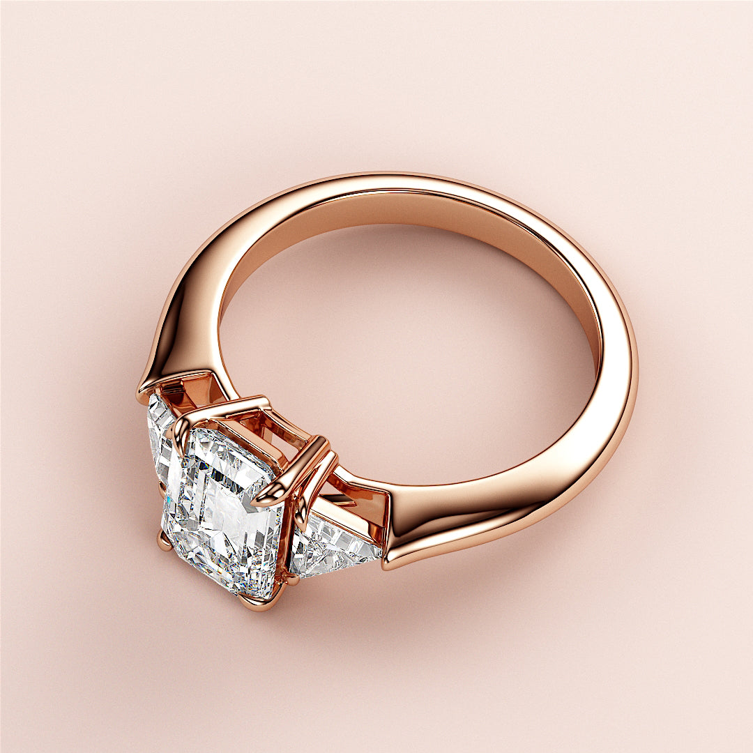 Elegant 14K rose gold engagement ring with emerald three-stone triangle design, featuring a stunning Asscher-cut diamond.