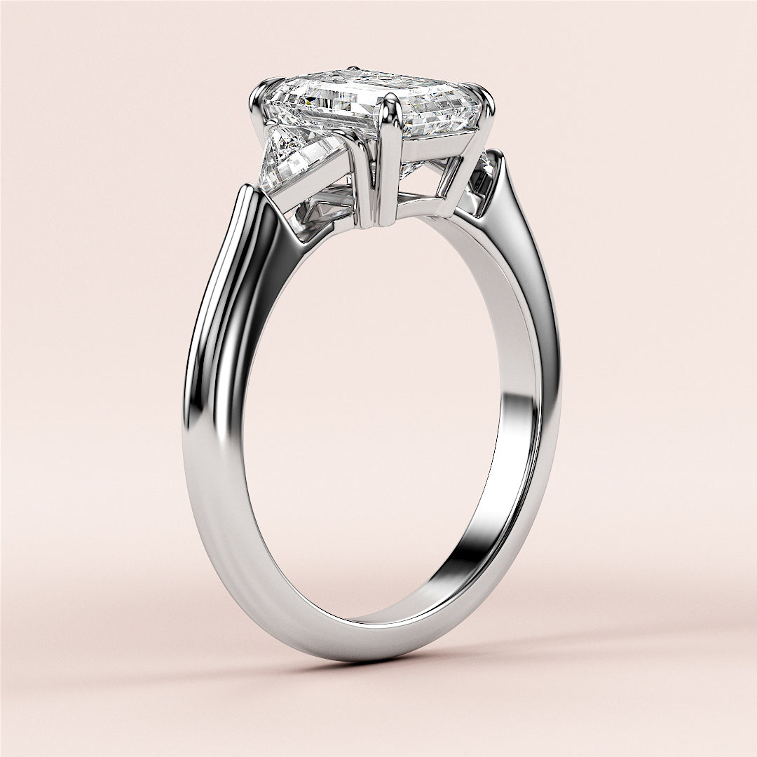 Emerald three-stone triangle engagement ring in 14K white gold, featuring intricate prong settings and a sleek band design.