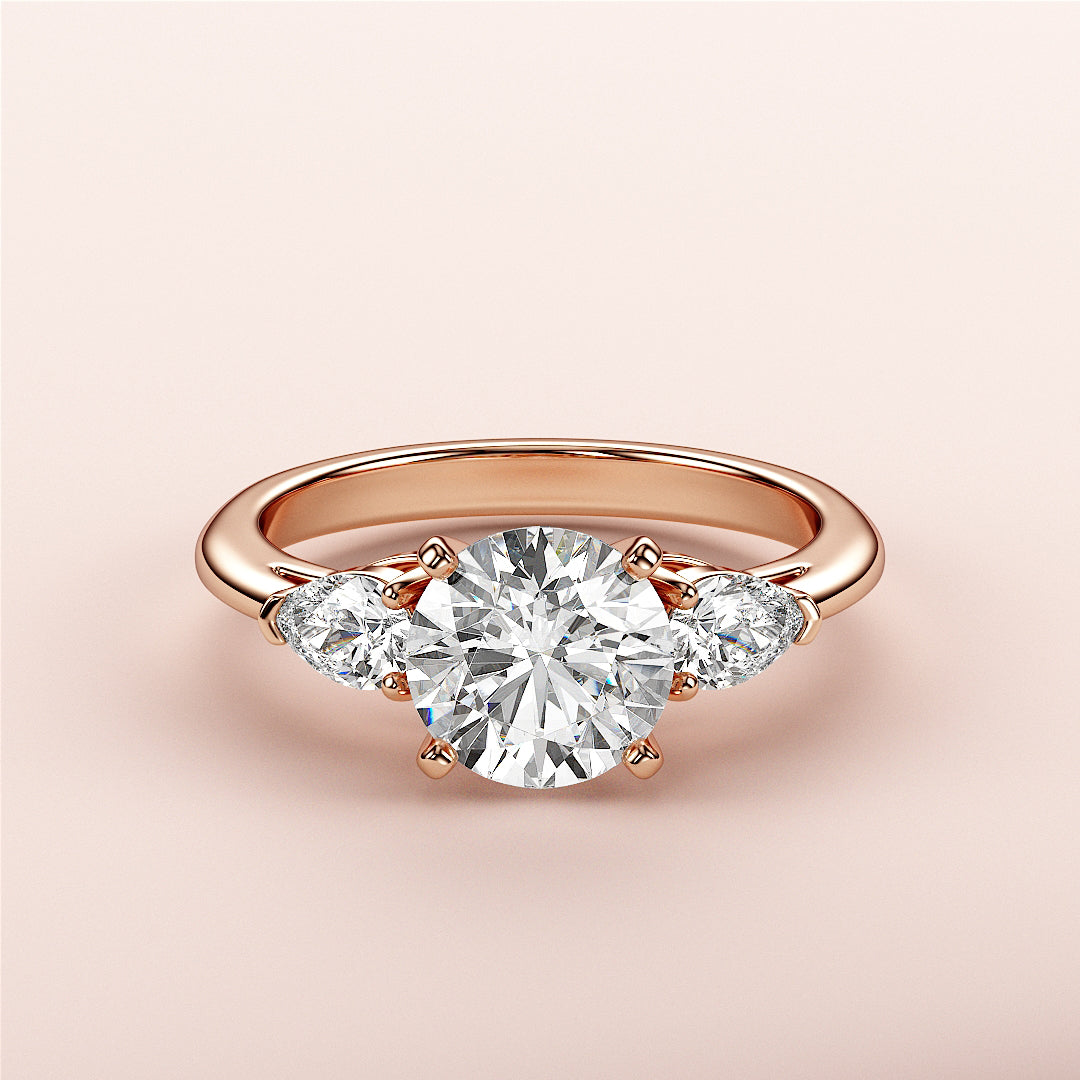 Elegant 14K rose gold engagement ring with round diamond center and two pear-shaped diamonds, perfect for timeless romance.