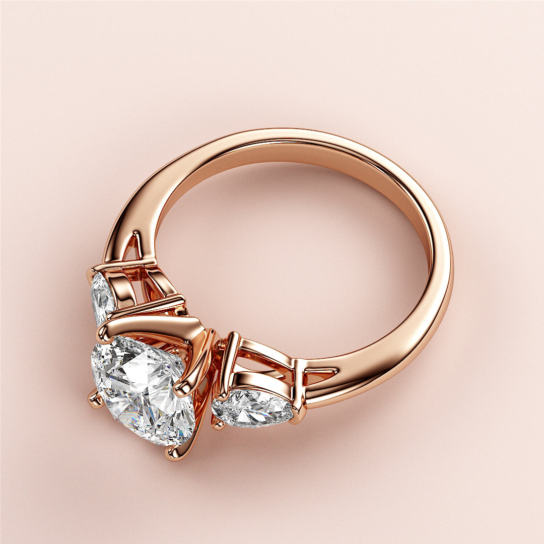 Close-up of an elegant 18K rose gold three-stone engagement ring with a round diamond and two pear-shaped diamonds.