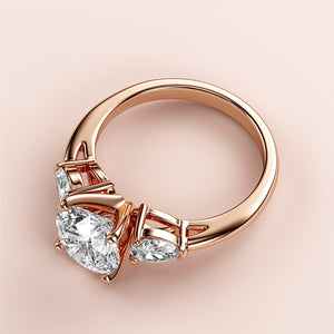 Close-up of an elegant 18K rose gold three-stone engagement ring with a round diamond and two pear-shaped diamonds.