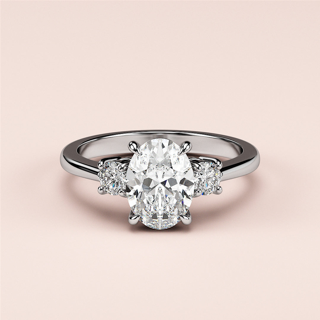 Elegant 14K/18K white gold three-stone engagement ring with oval and round diamonds on a soft pink background.|

#14KRecycledWhiteGold
#18KRecycledWhiteGold








#Platinum