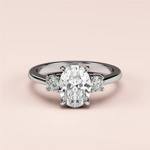 Elegant 14K/18K white gold three-stone engagement ring with oval and round diamonds on a soft pink background.