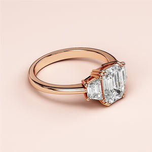 Elegant emerald cut diamond ring in rose gold, featuring three stones. Available in 14K, 18K, or platinum. Timeless design.