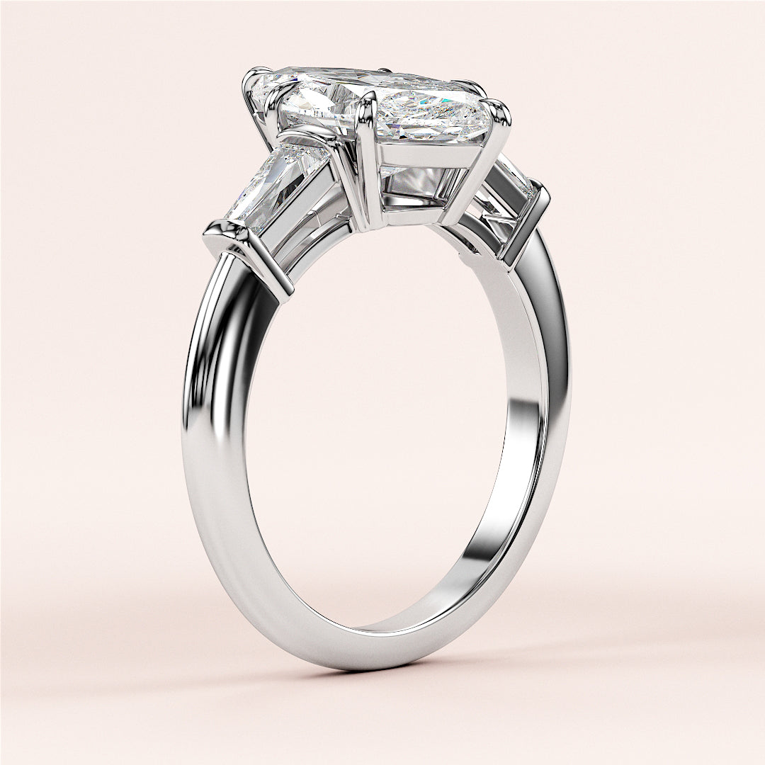 Elegant three-stone engagement ring in 14K/18K white gold, featuring a radiant-cut center diamond and trapezoid-cut side stones.