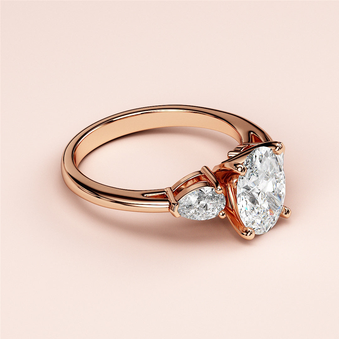 Elegant oval three-stone diamond engagement ring with pear-shaped side stones in 14K or 18K rose gold or platinum.