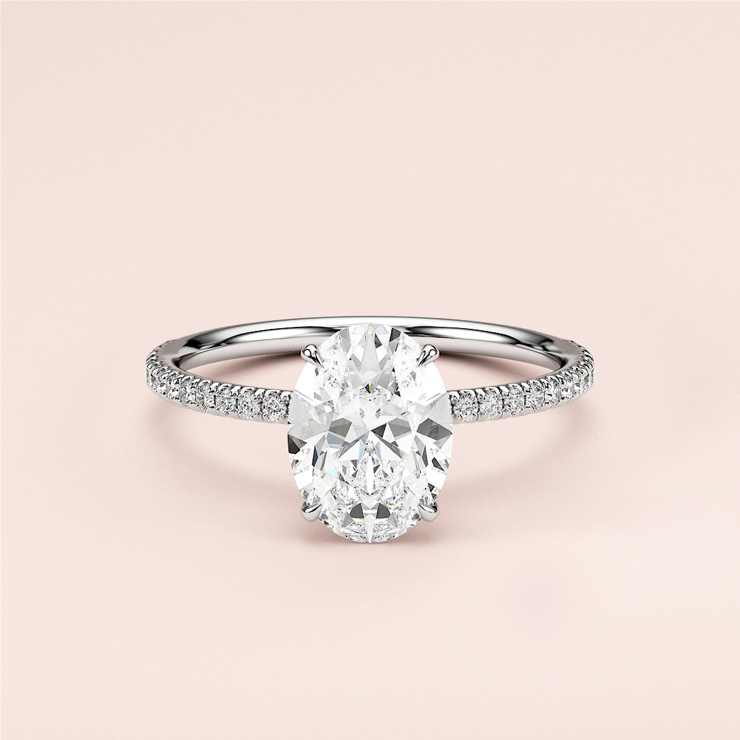 Elegant oval-shaped diamond engagement ring in 14K or 18K gold, featuring a delicate pave band against a soft background.
