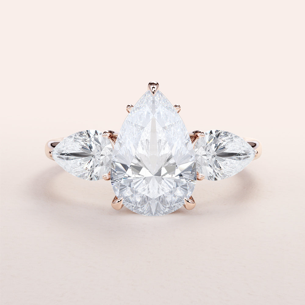 Three-stone pear-shaped diamond ring in 14K or 18K rose gold, featuring elegant side stones for a captivating engagement look.