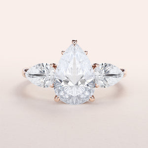 Three-stone pear-shaped diamond ring in 14K or 18K rose gold, featuring elegant side stones for a captivating engagement look.
