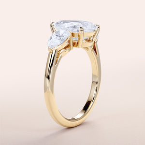 Elegant three-stone engagement ring in 14K or 18K yellow gold, featuring an oval diamond with pear side stones.