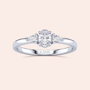 Elegant 14K or 18K gold three-stone engagement ring with oval diamond and pear-shaped accents on a cream background.